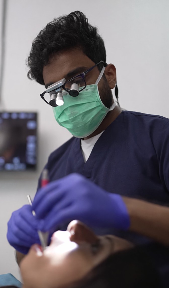 Dentist wearing a green mask and magnifying loupes performing a dental procedure on a patient.