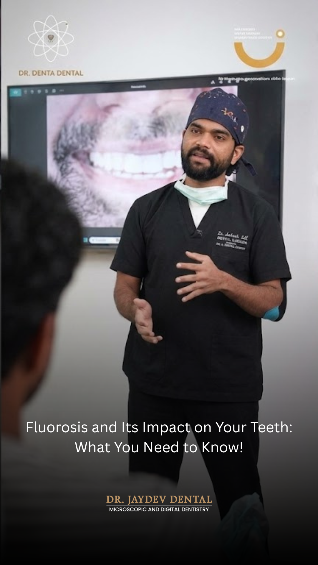 Dentist in scrubs giving a talk in front of a screen showing a teeth image, with 'Dr. Jaydev Dental' branding visible on the wall and screen behind him.