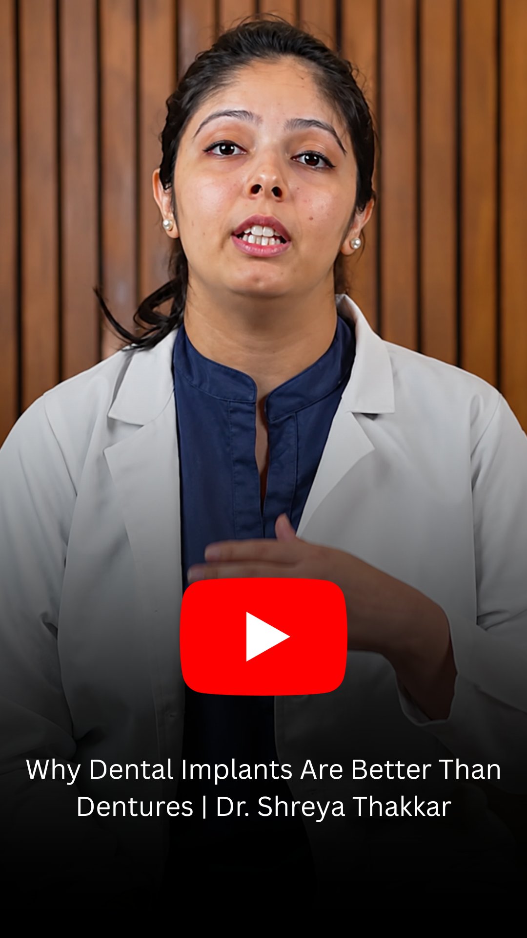 Video thumbnail featuring Dr. Shreya Thakkar in a white coat explaining why dental implants are better than dentures, with a YouTube play button overlay and the title text visible.