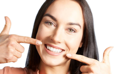 Smiling woman pointing to her teeth with both hands, highlighting her bright smile.