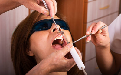 Child patient wearing protective goggles has mouth open during dental treatment, with dentist using instruments inside a clinic.